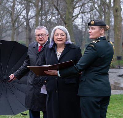 Her Excellency is walking in Green Park. A member of the military is holding a book in front of her. High Commissioner Ralph Goodale is to her right holding an umbrella.