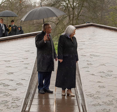 Son Excellence regarde un monument dans Green Park. Le haut-commissaire Ralph Goodale se tient à sa droite, tenant un parapluie.