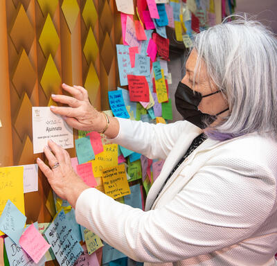 La gouverneure générale Mary Simon place son message à côté des autres sur un mur au pavillon de l'Ukraine. Le mur est couvert de post-it multicolores.