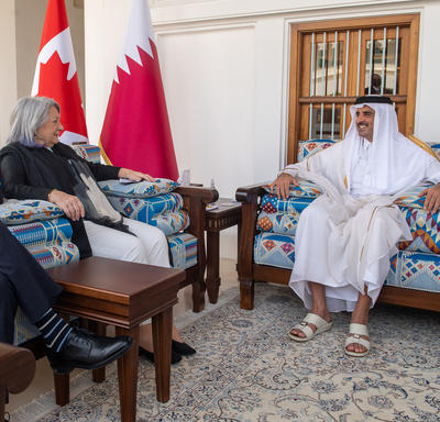 Governor General Simon and Mr. Whit Fraser are meeting with the Amir of Qatar. There is a flag of Qatar and a flag of Canada behind them.