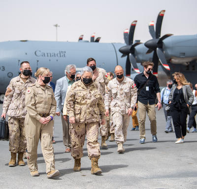 La gouverneure générale et un groupe de personnes marchent vers Camp Canada. Un avion militaire est derrière eux.