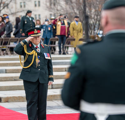 La gouverneure générale Simon salue. Elle est debout sur un petit podium devant le Monument commémoratif de guerre du Canada.