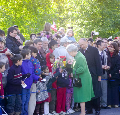The Queen, holding bouquets of flowers and wearing a green coat, greets a crowd of people outside Rideau Hall.