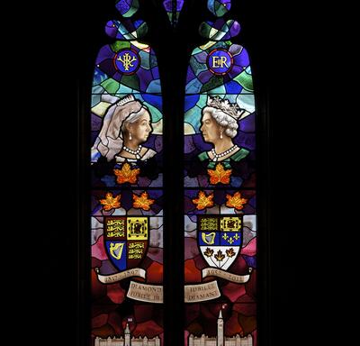Un vitrail comportant des images de la reine Victoria et de la reine Elizabeth II, la couronne royale, leurs monogrammes et armoiries respectifs et deux représentations du Parlement du Canada.