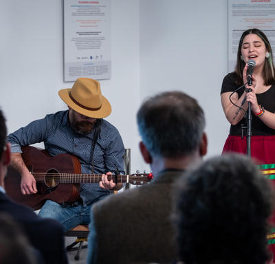 Une femme chante dans un micro tandis qu’un homme joue de la guitare.