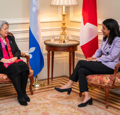 Governor General Mary Simon is pictured speaking to a woman. The Quebec flag and the Canadian flag are in the background. 