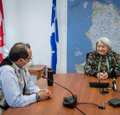 La gouverneure générale est assise à une grande table de conférence. Elle parle avec un homme.