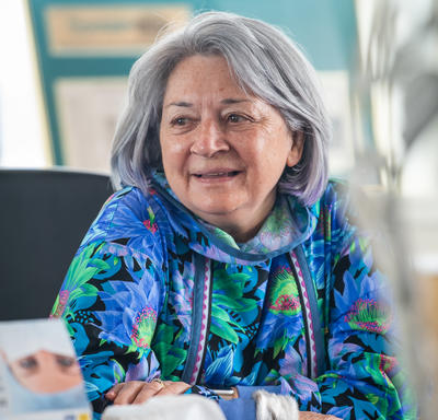 La gouverneure générale est assise à une table, souriante.