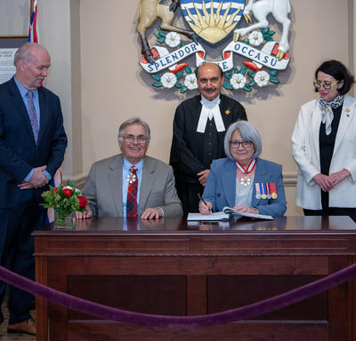 Their Excellencies are sitting behind a table. Premier of British Columbia, John Horgan, Speaker of the Legislative Assembly of British Columbia, Raj Chouhan, and Lieutenant Governor, Janet Austin are standing.