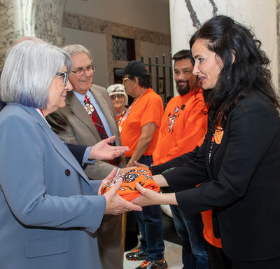 A woman is handing Governor General Simon an orange shirt.