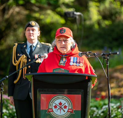 Governor General Simon is standing at a podium. She is speaking into a microphone. She is wearing a Canadian Rangers uniform. A woman wearing a military uniform is standing behind her.