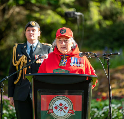 Governor General Simon is standing at a podium. She is speaking into a microphone. She is wearing a Canadian Rangers uniform. A woman wearing a military uniform is standing behind her. 