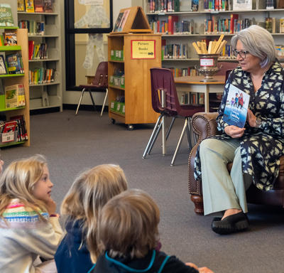 Governor General Simon is presenting a book to a group of children. They are sitting in a library.