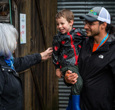Governor General Simon is speaking with a man holding a child. She is extending her hand towards the child who is smiling.