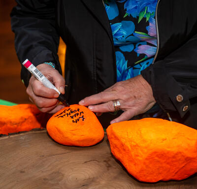 Governor General Simon is writing on an orange stone. The message reads, “Let’s walk together.” There is a line in Inuktitut under the English sentence.