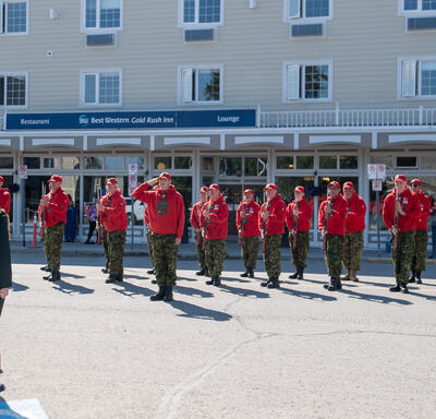 La gouverneure générale Simon est debout sur une petite plateforme légèrement surélevée. Une femme portant un uniforme militaire se trouve derrière elle, à sa droite. Elles font face à une garde d'honneur composée de Rangers canadiens.