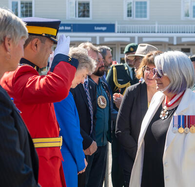 A man in uniform is saluting the Governor General as she greets a row of people.