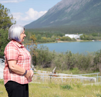 La gouverneure générale Simon est debout à l'extérieur. Elle regarde le lac et la montagne en face d'elle.