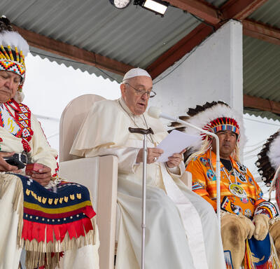 Le pape François prononce une allocution. Il est flanqué de deux chefs autochtones.