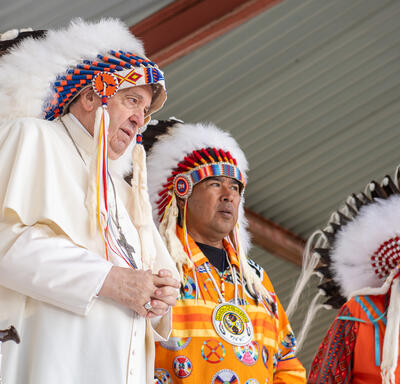 Le pape François porte une coiffe autochtone. Des chefs autochtones se tiennent autour de lui.