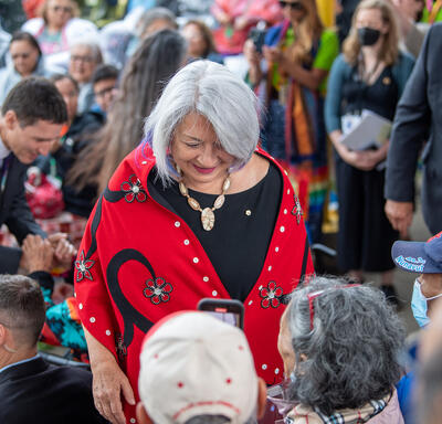 Governor General Simon is smiling as she stops to speak to people seated in an audience.