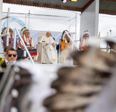 Pope Francis is seated on stage with Indigenous leaders.