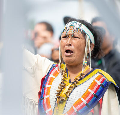 A woman dressed in traditional Indigenous clothing is crying out.
