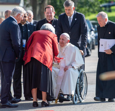 Pope Francis is being wheeled in a wheelchair across the grounds of the GGCitadelle. Governor General Simon is greeting him.