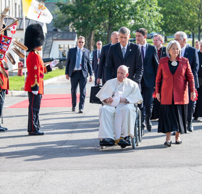 Le pape François est transporté en fauteuil roulant sur le terrain de la GGCitadelle. La gouverneure générale Simon, le premier ministre Justin Trudeau et plusieurs autres personnes marchent derrière lui.