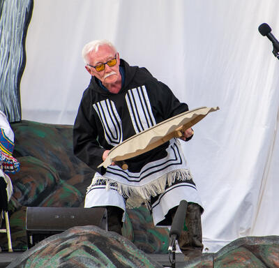 A man wearing traditional Inuit clothing plays a qilaut. 