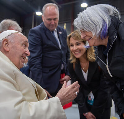 Le pape François et la gouverneure générale Simon se font face. Ils parlent et sourient. Il y a des gens autour d'eux.