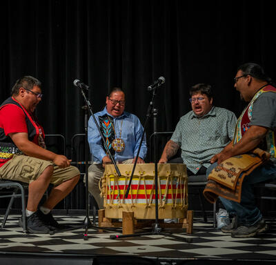Four individuals are performing on stage. They are positioned around a large drum.