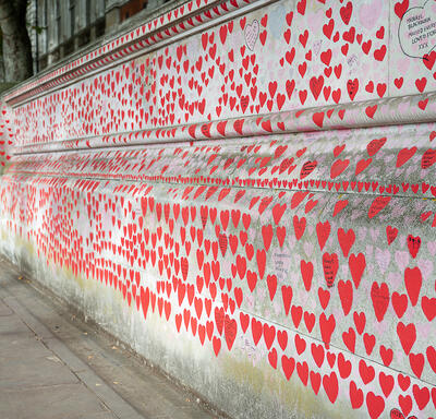 Thousands of small red hearts with printed messages are painted on a concrete wall. 