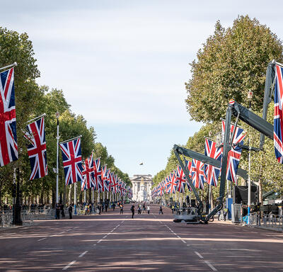Une large rue bordée de drapeaux du Royaume-Uni. Des personnes se trouvent sur le côté gauche de la rue. Certaines personnes traversent la rue.