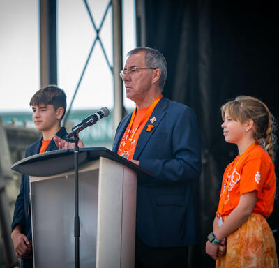 Le lieutenant-gouverneur de la Saskatchewan, Russ Mirasty, est sur scène avec des étudiants de chaque côté de lui.