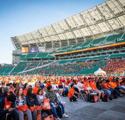 Un groupe d'étudiants portant des chandails orange se tient sur le sol d'un stade.