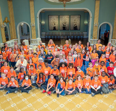 La gouverneure générale Simon et M. Fraser posent pour une grande photo de groupe avec des écoliers dans la salle de bal de Rideau Hall. La plupart des enfants portent un chandail orange.