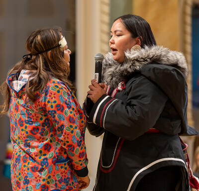 Two throat singers are performing in the Ballroom at Rideau Hall. Schoolchildren are seated around them, watching.