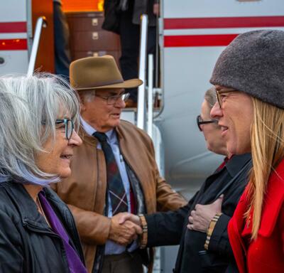 La gouverneure générale parle à l'ambassadrice canadienne en Islande, Jeannette Menzies. M. Fraser et trois autres personnes se tiennent derrière eux sur le tarmac. Le côté d'un avion est visible derrière eux.