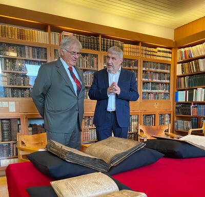 Mr. Fraser is standing next to Mr. Gudvardur Mar Gunnlaugsson. They are talking. A large manuscript with weathered pages is open in front of them.