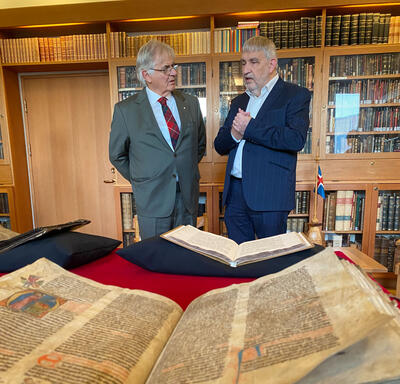 Mr. Fraser is standing next to Mr. Gudvardur Mar Gunnlaugsson. They are talking. A large manuscript with weathered pages is open in front of them.