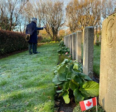 M. Fraser et le colonel Ronald Walker se trouvent dans un cimetière. Il y a une rangée de pierres tombales en pierre grise devant eux.