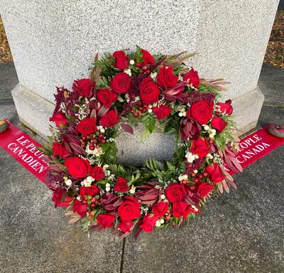A wreath leaning against a memorial in Fossvogur Cemetery. Text on a red ribbon next to the wreath reads, “The people of Canada.”