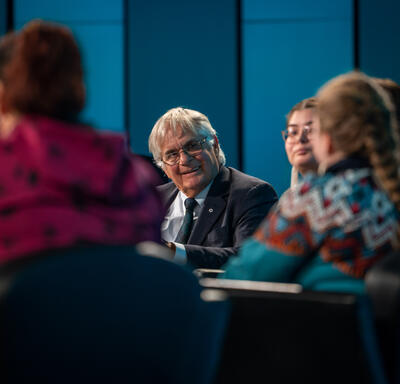 Mr. Fraser is smiling at panelists. The photo is taken from behind two panelists.