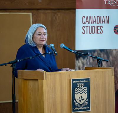 The Governor General is standing at a podium. A slide with the words ‘Canadian Studies’ is to her left.