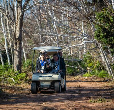 La gouverneure générale est conduite à travers les bois dans une voiturette de golf.