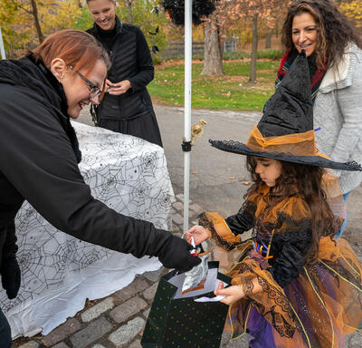 A child dressed as a witch is receiving candy in a bag.