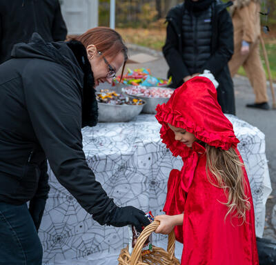 A young child wearing a red cap is receiving Halloween treats.