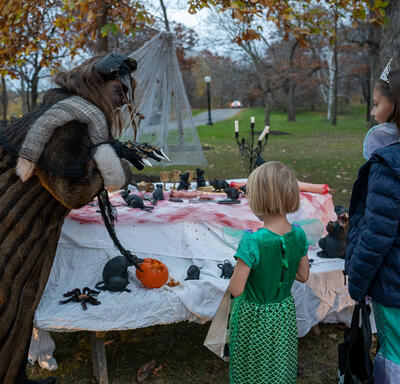 Young kids dressed up for Halloween are looking at a table with Halloween displays.