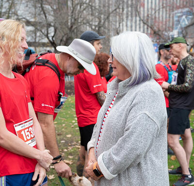 Governor General Mary Simon is speaking with a participant of the Army Run. They are standing outside and there are many other participants around them. 